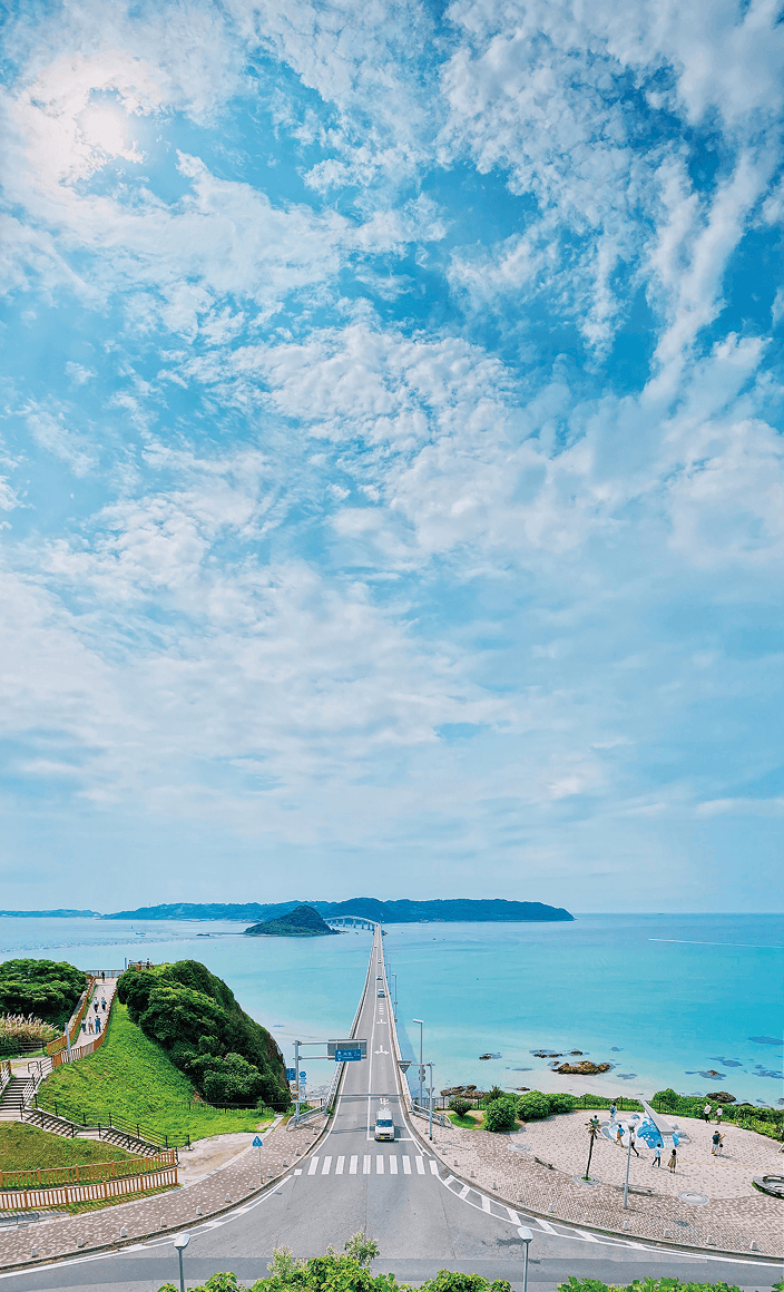 坂の上からパノラマで撮られた海に向かって続く長い一本道の写真