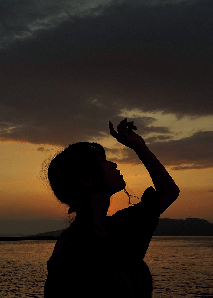 海を背景にしてポーズをとる女性の写真の明るさを暗くして幻想的にした写真