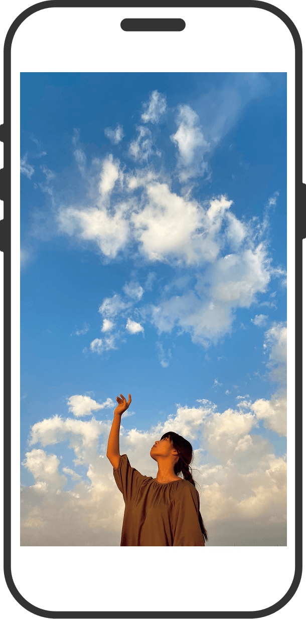 スマホ画面に映る、青空の下で空に向かって手を上げる女性の写真