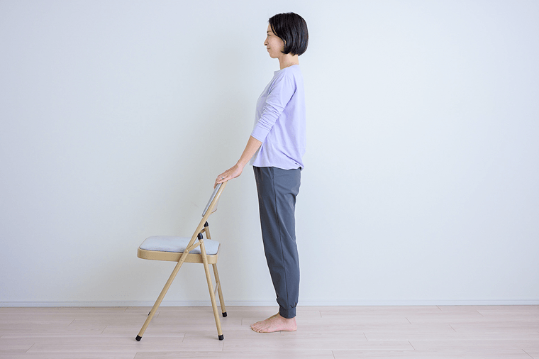 両手を肩幅に開いて椅子の背もたれの上を持って立つ先生