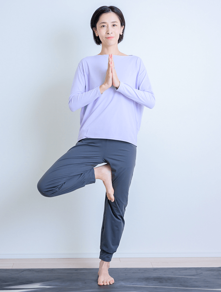 手のひらを胸の前で合わせ上げた足の裏を反対側の足に添える先生