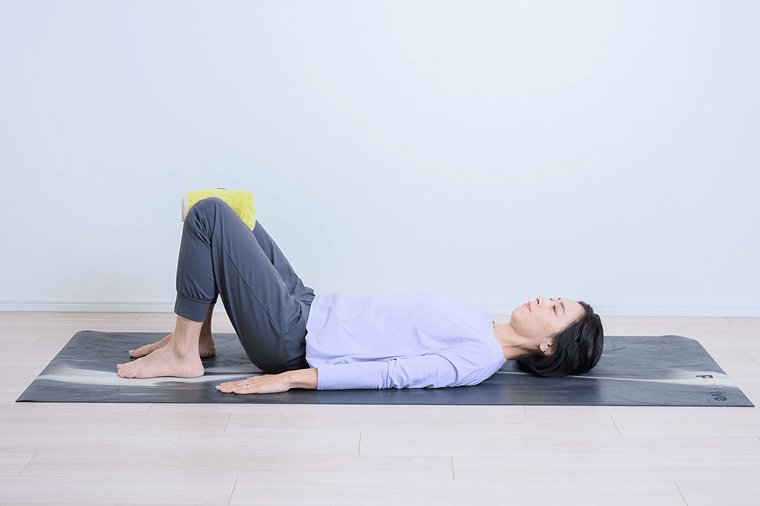 仰向けで膝を立てタオルを膝の間に挟む先生