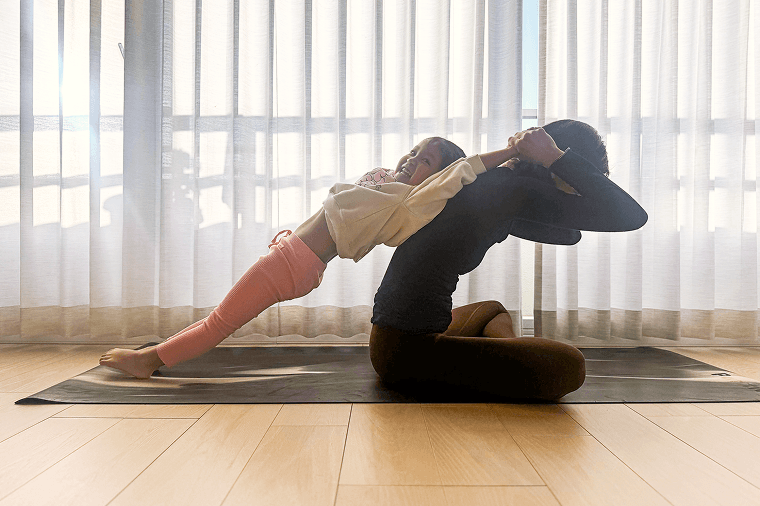 腕を伸ばす子供の手首を支えながら背中に寄りかかってもらう親